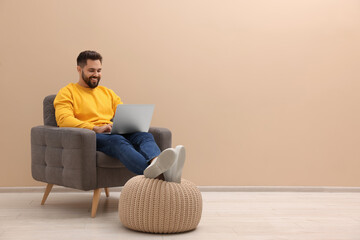 Poster - Handsome man with laptop sitting in armchair near beige wall indoors, space for text