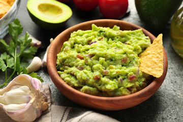 Wall Mural - Delicious guacamole with nachos chips and ingredients on grey table, closeup