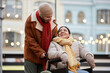 © Seventyfour - Portrait of young couple with smiling woman using wheelchair enjoying date outdoors in Christmas city