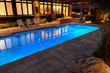 Home with outdoor patio and lights on at night and blue lit swimming pool with stone deck