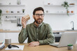 © sofiko14 - Caucasian bearded man in eyeglasses and looking at small cardboard parcel with focused facial expression. Social media influencer streaming unpacking process of online order from home.
