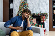 © Liubomir - New Year's celebration and Christmas, man has severe stomach pain, hispanic sitting on sofa in living room, massaging stomach with hand.