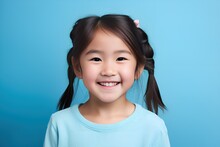 Close-Up Portrait Of A Fictional Young Asian Little Girl Wearing Casual Blue T-Shirt And Smiling. Isolated On A Plain Blue Background. Generative AI.