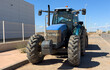 Farm tractor parked at warehouse on construction site. Tractor with trailer with water in barrel for watering and moisturizing asphalt road. Blue agricultural tractor with trailer with fertilizers