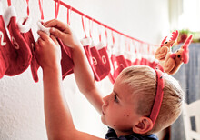 A Young Boy With Festive Reindeer Antlers Retrieves A Gift From A Red Numbered Christmas Stocking On A White Wall. His Anticipation Of The Day's Surprise Embodies The Holiday Spirit. Advent Calendar