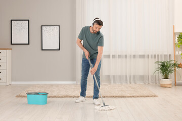 Sticker - Enjoying cleaning. Man in headphones listening to music and mopping floor at home