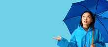 Beautiful Young Asian Woman In Raincoat Holding Umbrella On Light Blue Background With Space For Text