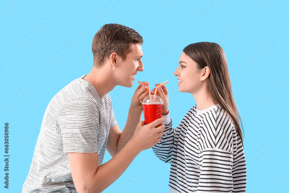 Happy young couple drinking soda on blue background