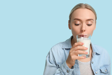 Wall Mural - Pretty young woman drinking milk on blue background