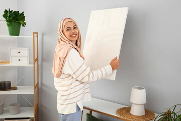 Sticker - Young Muslim woman hanging painting on light wall at home