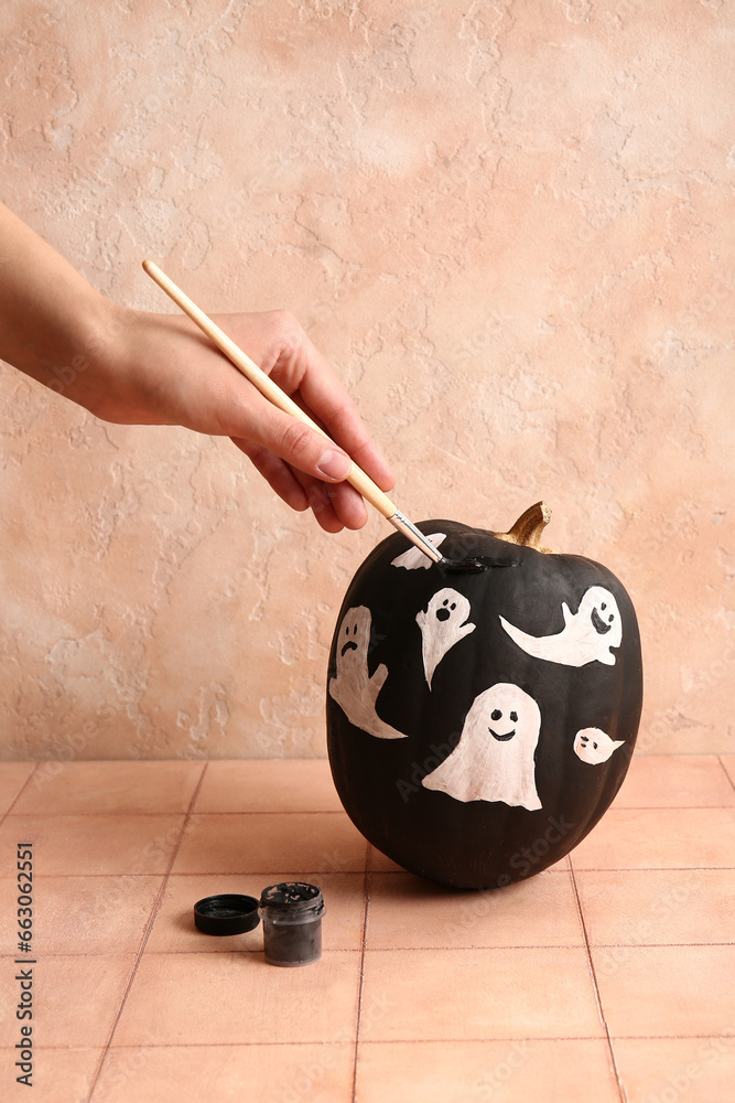 Woman painting Halloween pumpkin with ghosts on beige tiled table