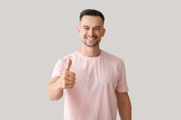 Canvas Print - Happy young man showing thumb-up on light background