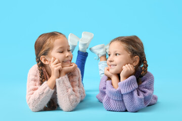 Poster - Cute little girls in warm sweaters lying on blue background