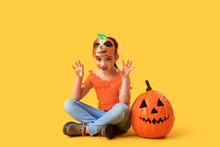 Little Girl Dressed For Halloween With Pumpkin On Yellow Background