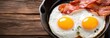 Two fried eggs and bacon in a frying pan against a wooden background.