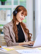 © Bangkok Click Studio - Asian professional successful young female businesswoman creative graphic designer in casual outfit sitting smiling wearing headphone listening to music playlist while working typing laptop computer