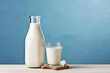 A bottle of milk and a glass of milk on a wooden table on a blue background.