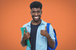 Successful black male student with beard showing thumb up on orange background