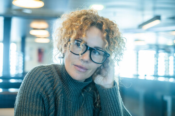 Portrait of cute pretty woman smiling indoor inside cafe bar wearing glasses. Middle age beauty female people with curly hair. Serene expression person in interior leisure relax activity alone