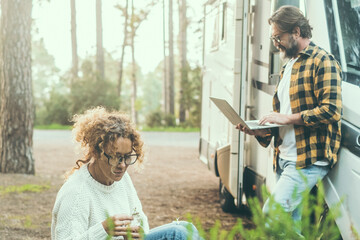 Wall Mural - Travel couple adult people man and woman enjoy outdoor leisure activity outside a modern rv vehicle camper van parking in the forest. Adventure traveler vanlife lifestyle. Digital nomad using computer