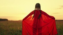Cute little girl with braids wearing red cloak plays hero in sunset summer meadow