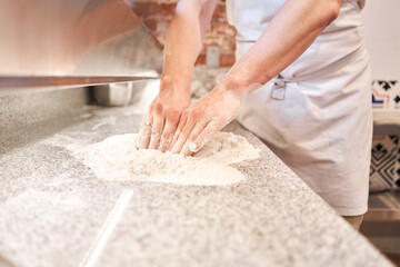 Wall Mural - The chef prepare pizza. Raw pizza ready to bake. Cook in a apron in the kitchen Rolls out pizza dough. boxes for food delivery on background.