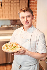 Wall Mural - The chef holds a pizza in his hands. Neapolitan pizza from a wood-fired oven. Pizza is on the plate. Pizza with pear and gorgonzola. Fast delivery of food. 