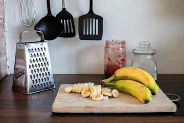 Wall Mural - Whole and sliced ​​bananas on the kitchen table. Various kitchen utensils in the background