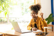 © ArLawKa - Young African American girl wearing headphones, smartphone, video call on laptop, looking at computer screen, watching webinar or doing video chat by webcam, online work concept.