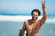 Surfing, portrait and happy man with peace hands at a beach for travel, freedom or adventure. Face, smile and male surfer with v sign at sea for water sports, training or summer vacation in Miami