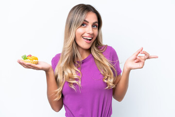 Wall Mural - Young pretty Uruguayan woman holding a tartlet isolated on white background surprised and pointing finger to the side