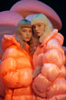 © Glittering Humanity - Two women radiate winter beauty in their puffy jackets, surrounded by neon mushroom lights, as they stand glowing with a fierce and vibrant energy