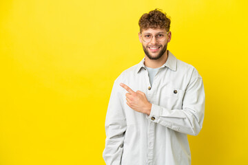 Wall Mural - Young handsome caucasian man isolated on yellow background pointing to the side to present a product