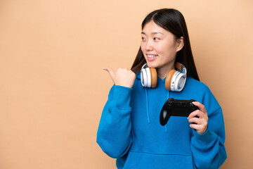 Wall Mural - Young Chinese man playing with a video game controller isolated on beige background pointing to the side to present a product