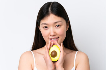 Wall Mural - Young Chinese woman isolated on white background holding an avocado while smiling. Close up portrait