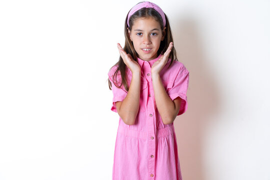 Surprised terrified Beautiful kid girl wearing pink dress Gestures with uncertainty, stares at camera, puzzled as doesn't know answer on tricky question, People, body language, emotions concept