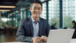 © PixelGallery - A smiling asian businessman is using a laptop in his office