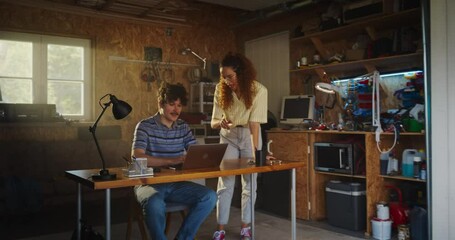 Poster - Caucasian Male Software Engineer And Hispanic Female User Interface Designer Talking And Using Laptop Computer in Garage At Home. Diverse Young Startup Founders Working On Innovative Online Service.