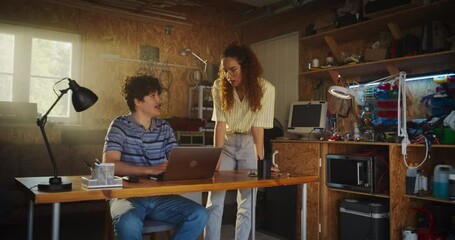 Poster - Caucasian Male Software Developer And Hispanic Female Business Partner Talking And Using Laptop Computer in Garage At Home. Diverse Young Startup Founders Working On Innovative Online Service.