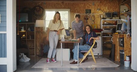 Fototapete - Diverse Team Of Three Young Startup Company Founders In Retro Garage With Old Desktop Computer. Male And Female Entrepreneurs Looking At Camera And Smiling. Developing Online Service In Nineties.