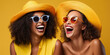 Portrait of two young women of different races laughing and having fun together on a yellow background