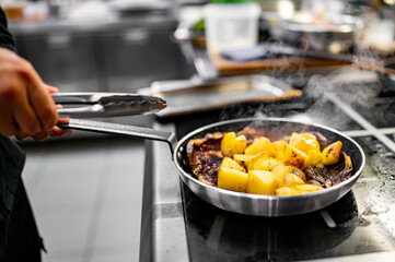 Wall Mural - Chef cook hand cooking potato and meat food in pan at the restaurant kitchen