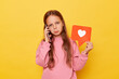 Unhappy sad little girl wearing pink sweatshirt standing isolated over yellow background talking on mobile phone sharing bad news showing blogger heart icon nobody appreciate her content.