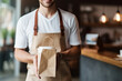 handsome smiling young barista holding coffee to go in paper cup and take away food in paper bag