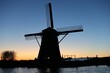 © Wirestock - Majestic windmill illuminated in the sky as the sun sets over a tranquil body of water