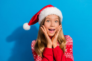 Sticker - Portrait of overjoyed teen girl wear jumper santa hat hold palms on cheekbones astonished staring isolated on blue color background