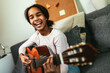 © Mediteraneo - African american teenage girl sitting on couch in her room and learning to play guitar