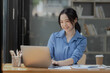 © SOMKID - Asian businesswoman working on laptop sitting at desk in office,