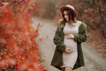 Stylish pregnant woman walks in an autumn park, happily expecting a baby. Happy pregnancy. Motherhood. Autumn season.