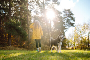 Wall Mural - Happy woman with her husky is walking in a green meadow, having fun. The owner of the pet spends time together. Concept of friendship, vacation, walk.